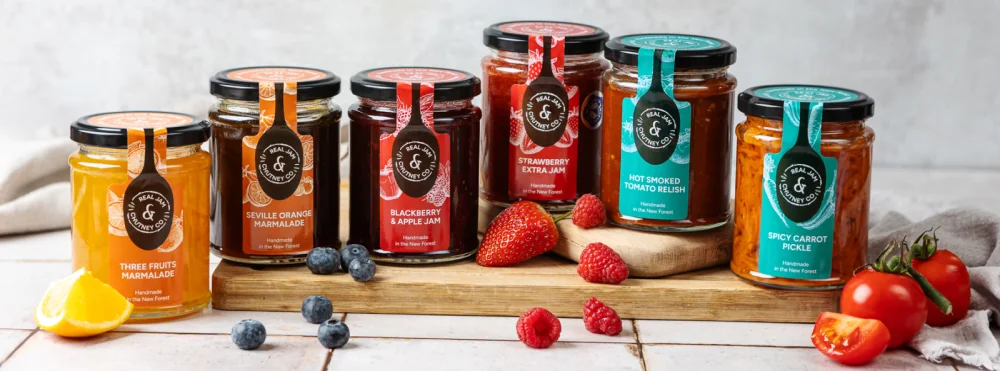 Jars of Real Jam and Chutney Company preserves beside fruit and tomatoes